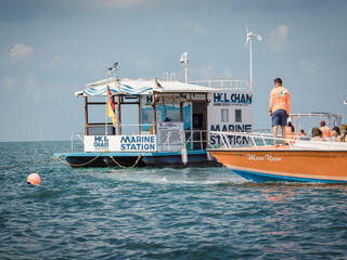 A floating ranger station is approached by an orange boat on a sunny day in Hol Chan, Belize