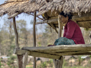 A person in brightly colored clothing sits on a raised platform looking out over the land on a sunny day