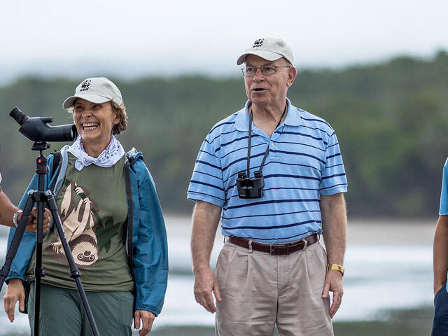 Four people stand on a low-tide beach. They all have big smiles. The NatHab guide is holding a telescope.