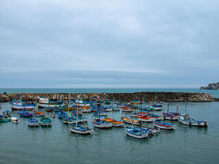 A group of small fishing boats gathers in a harbor in Peru on a cloudy day