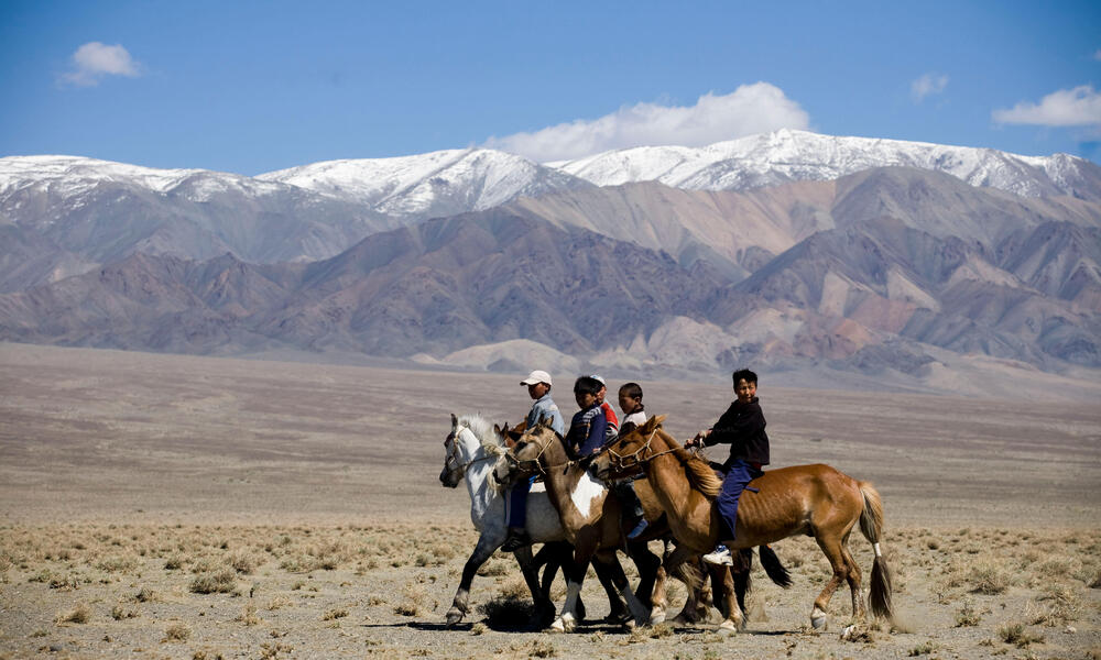 A group of children on horseback in a row in front of a large mountain range 