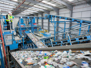 Two people stand on an elevated walkway overlooking a recycling plant