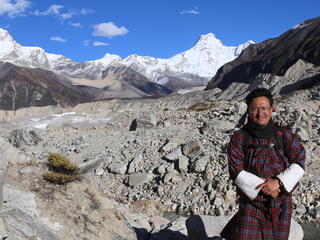 Dechen Dorji stands in front of tall snowy peaks on a sunny day