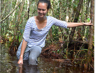 Stephanie Roe stands in wetland, leaning on tree