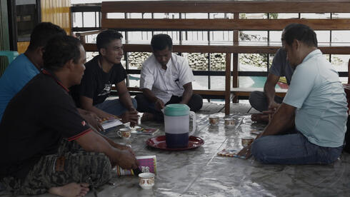 A group of men sit in a circle on a tile floor having a discussion