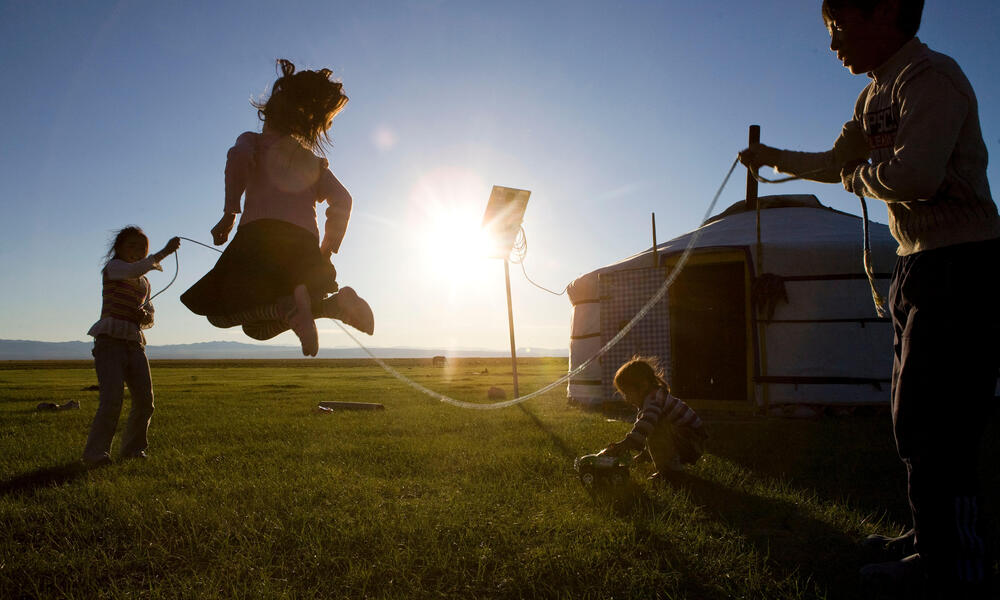 Three children jumping rope on the grass in the sunset